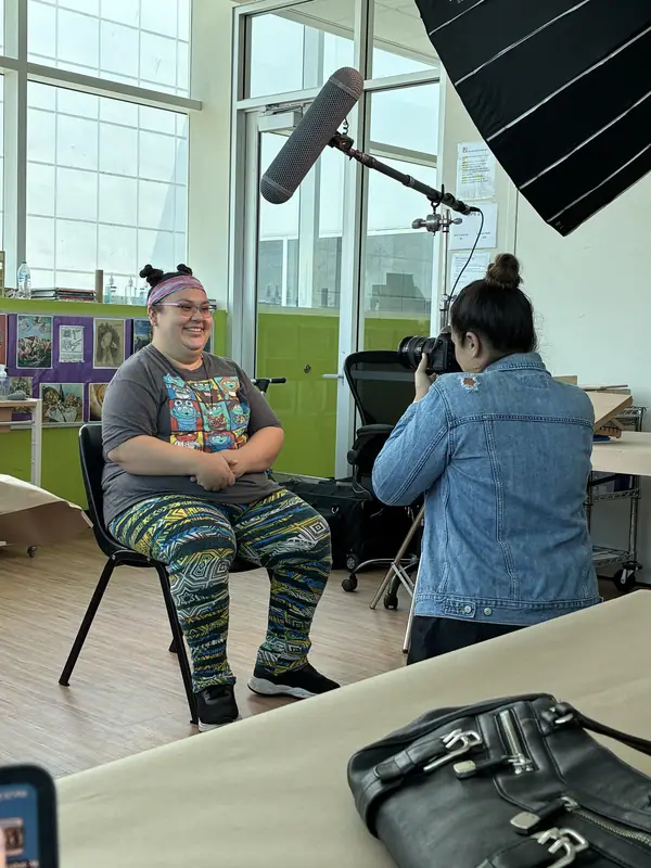 A storyteller sits smiling while a videographer films her during a workshop.