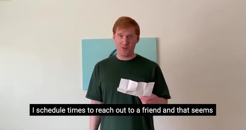 A storyteller in a green T-shirt reads from a folded sheet of paper in a video, with a caption along the bottom.